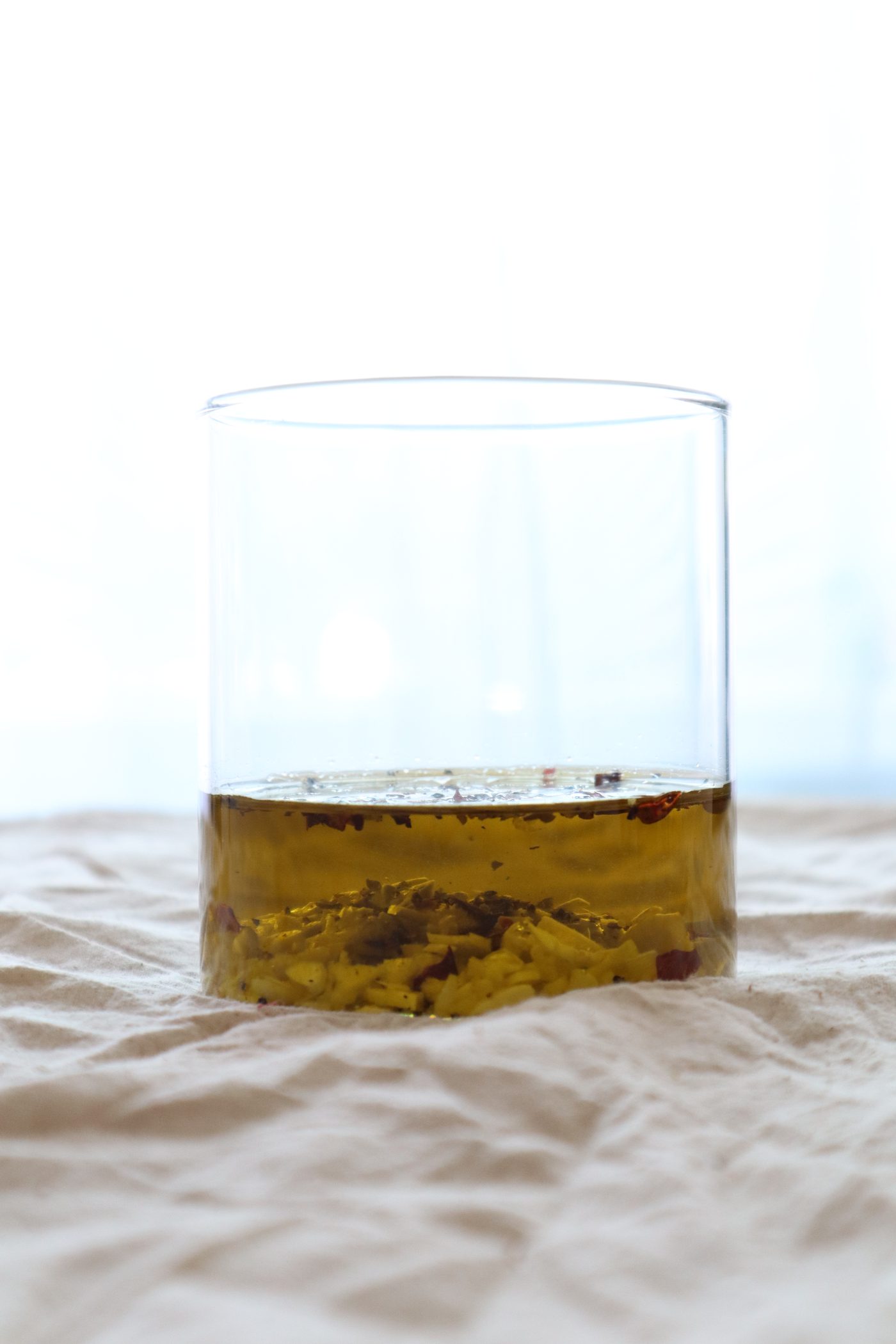 Close-up glass of infused olive oil with chili and herb sediment, backlit