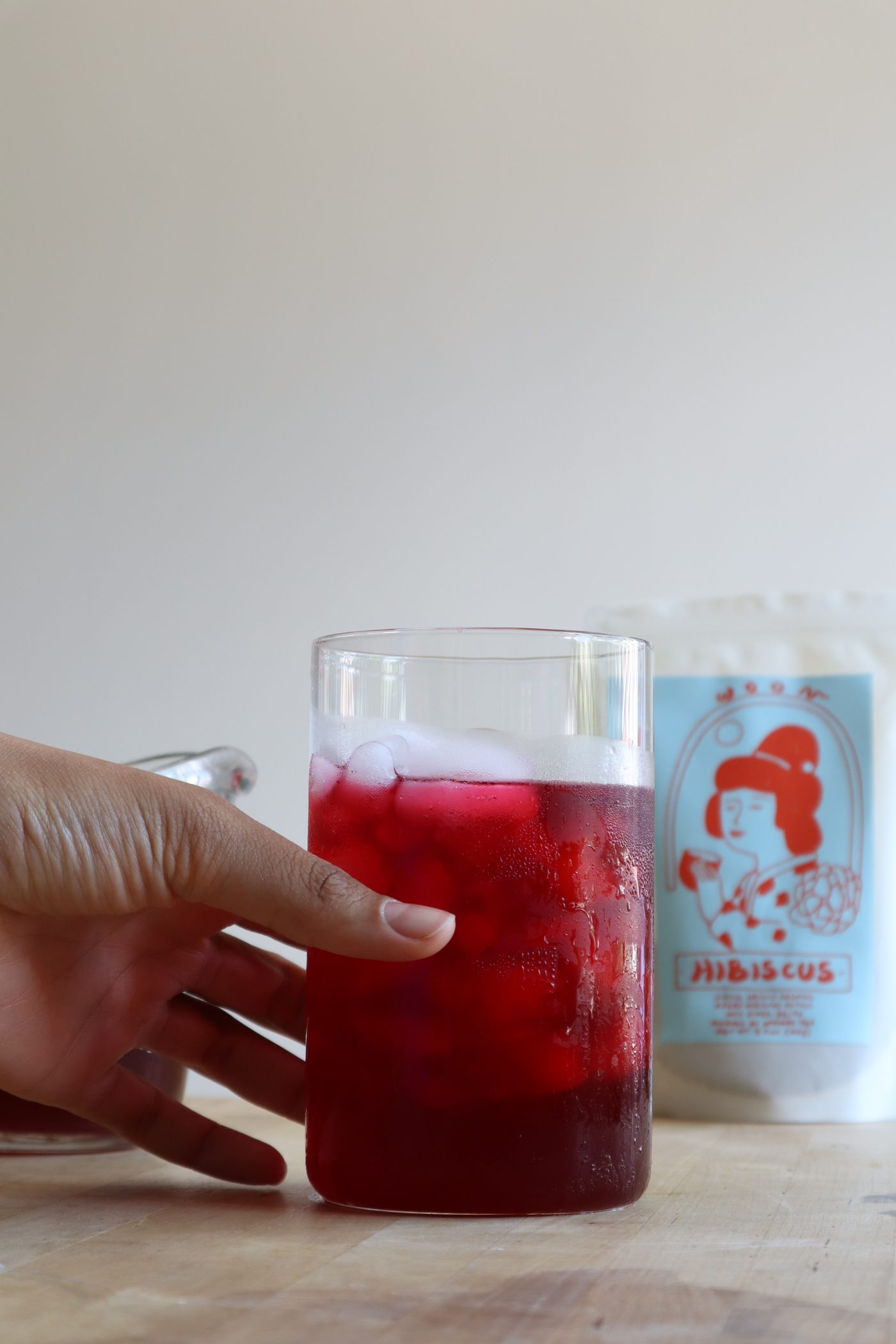 Hand reaching for a glass of iced hibiscus tea beside its packaging