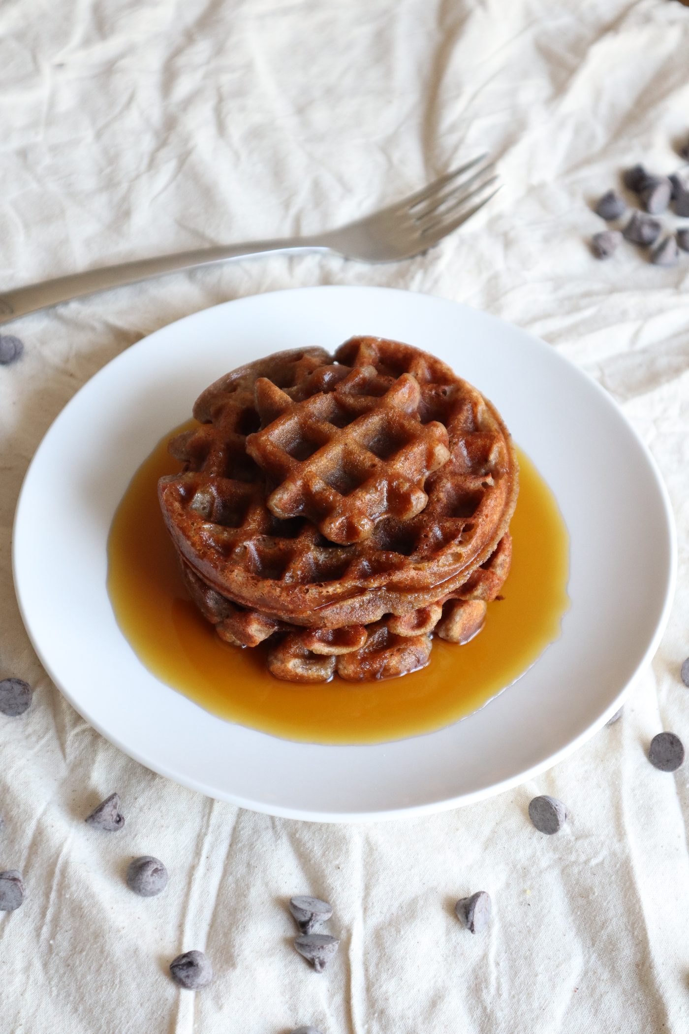 Stack of waffles topped with maple syrup, chocolate chips scattered around the plate