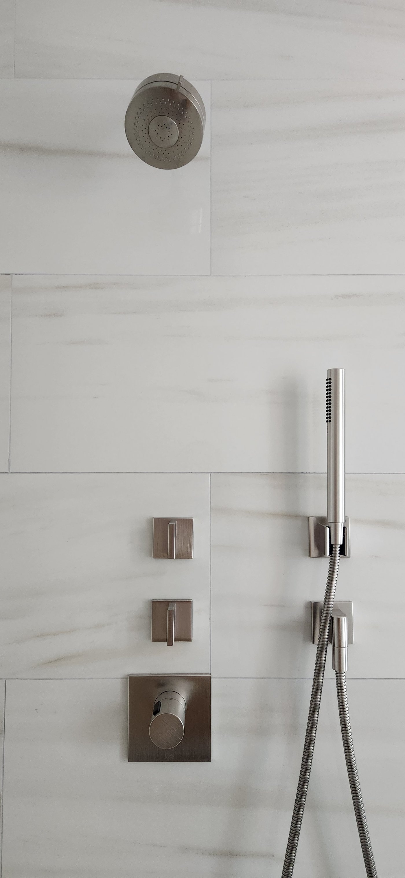 Brushed nickel shower system with handheld wand and thermostatic valves on marble tile
